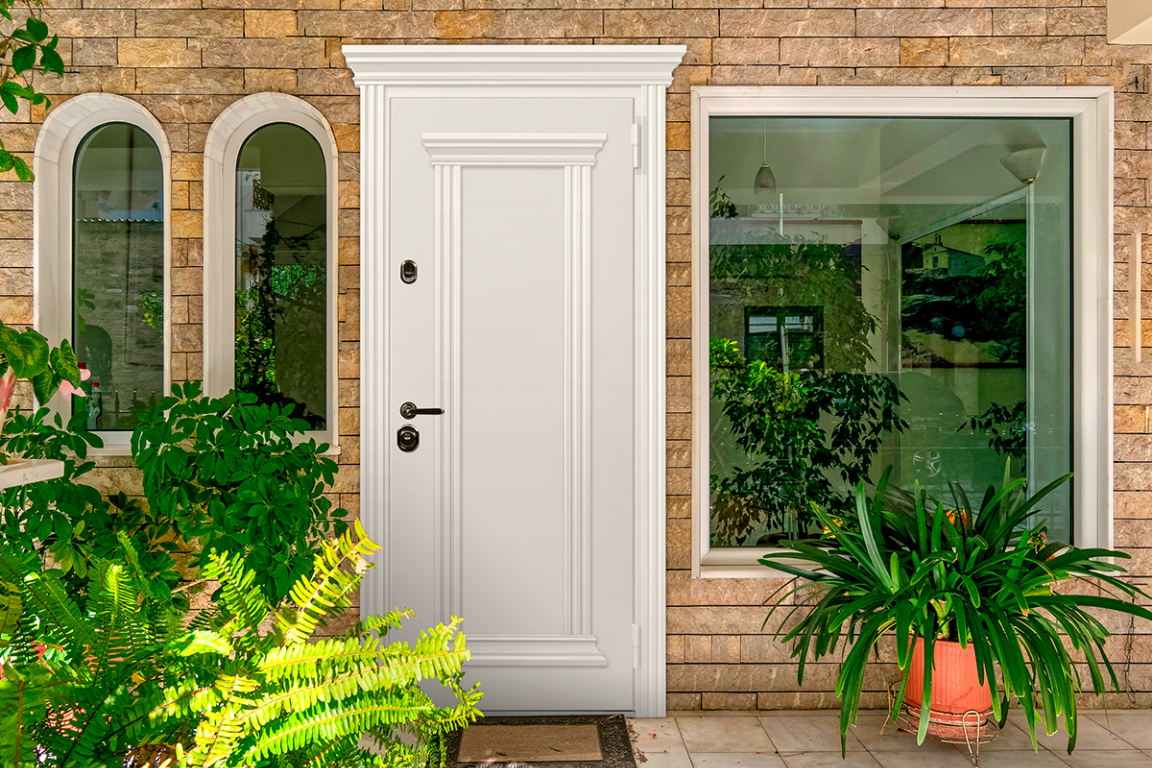 Входные двери с багетами белого цвета создают светлый акцент на фоне каменного фасада и зелени.