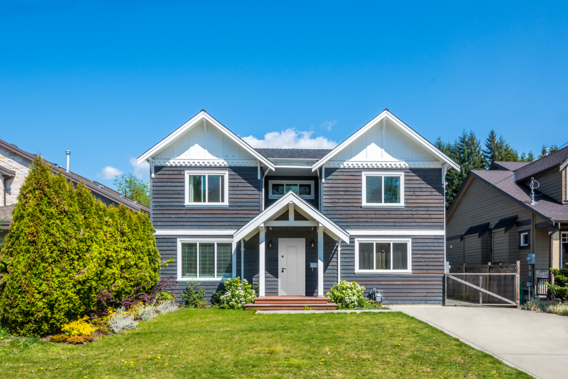 Входная дверь с багетами и белой отделкой, ведущая в двухэтажный дом с серым сайдингом.