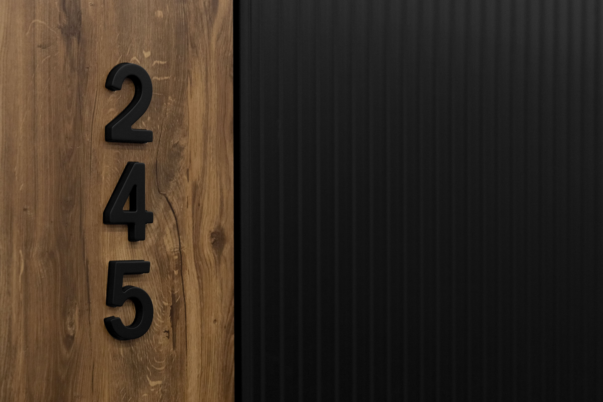 Номер на дверь выполнен в виде чёрных цифр, размещённых вертикально на деревянной вставке.