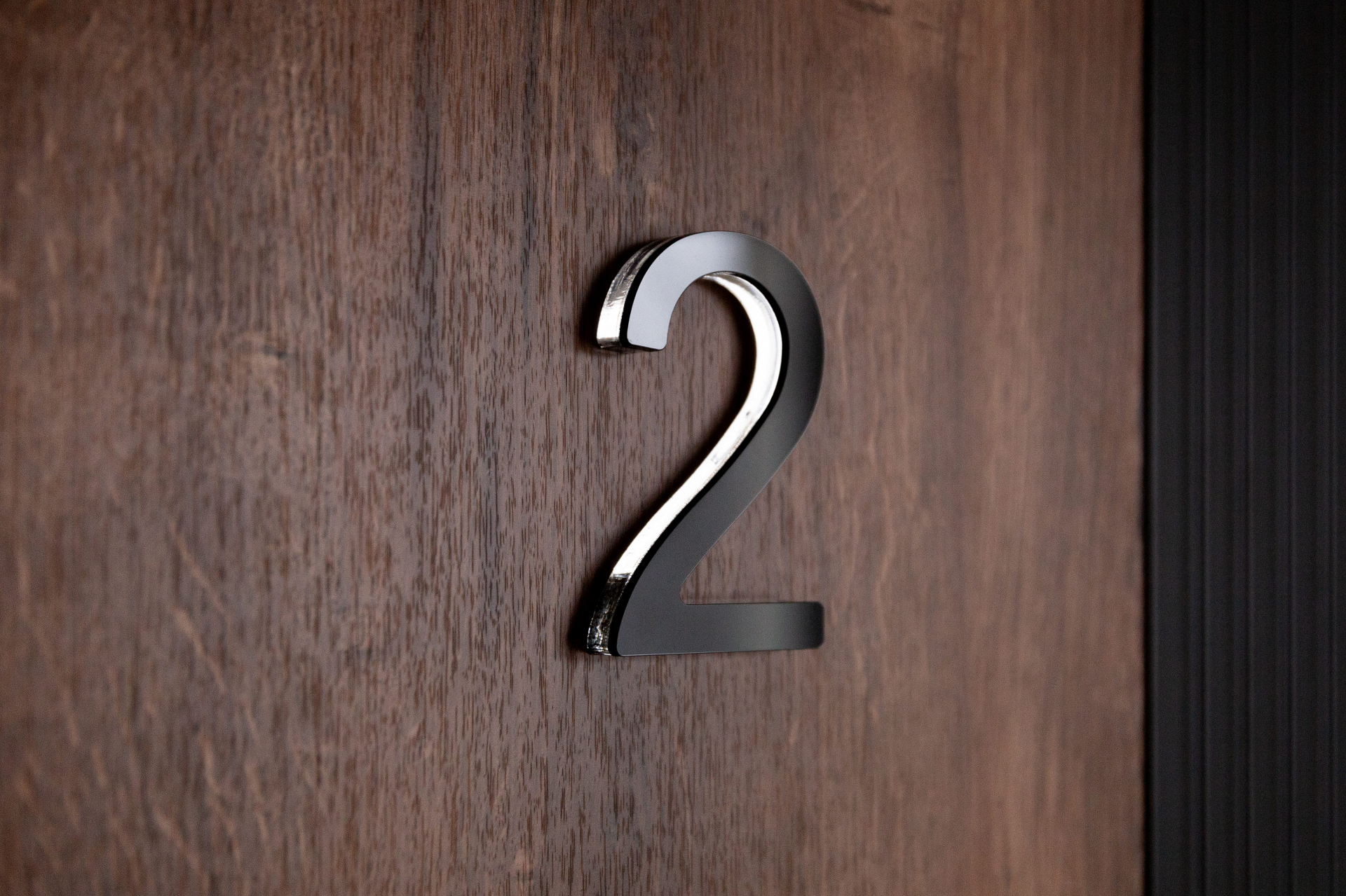 Цифра на дверь выполнена в объёмном металлическом исполнении и закреплена на деревянной панели.